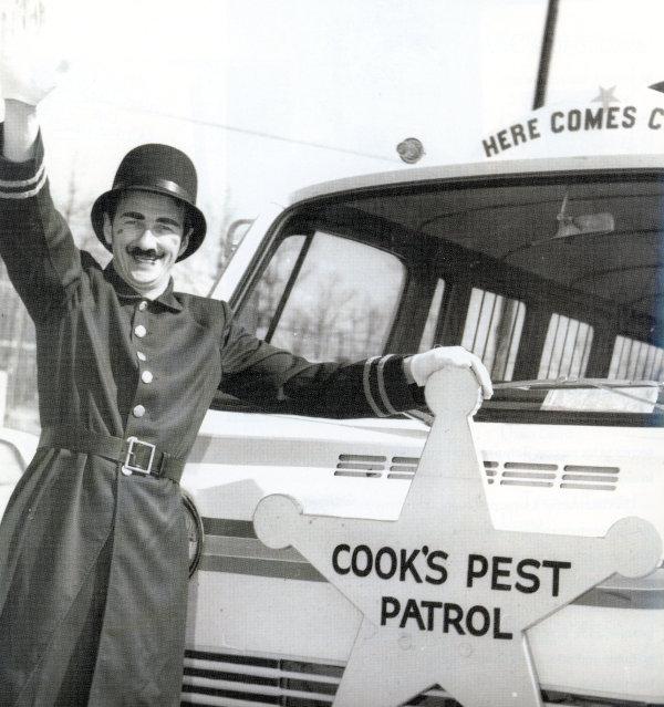 Vintage photo of a man in a top hat and uniform waving beside a Cook's Pest Patrol vehicle.