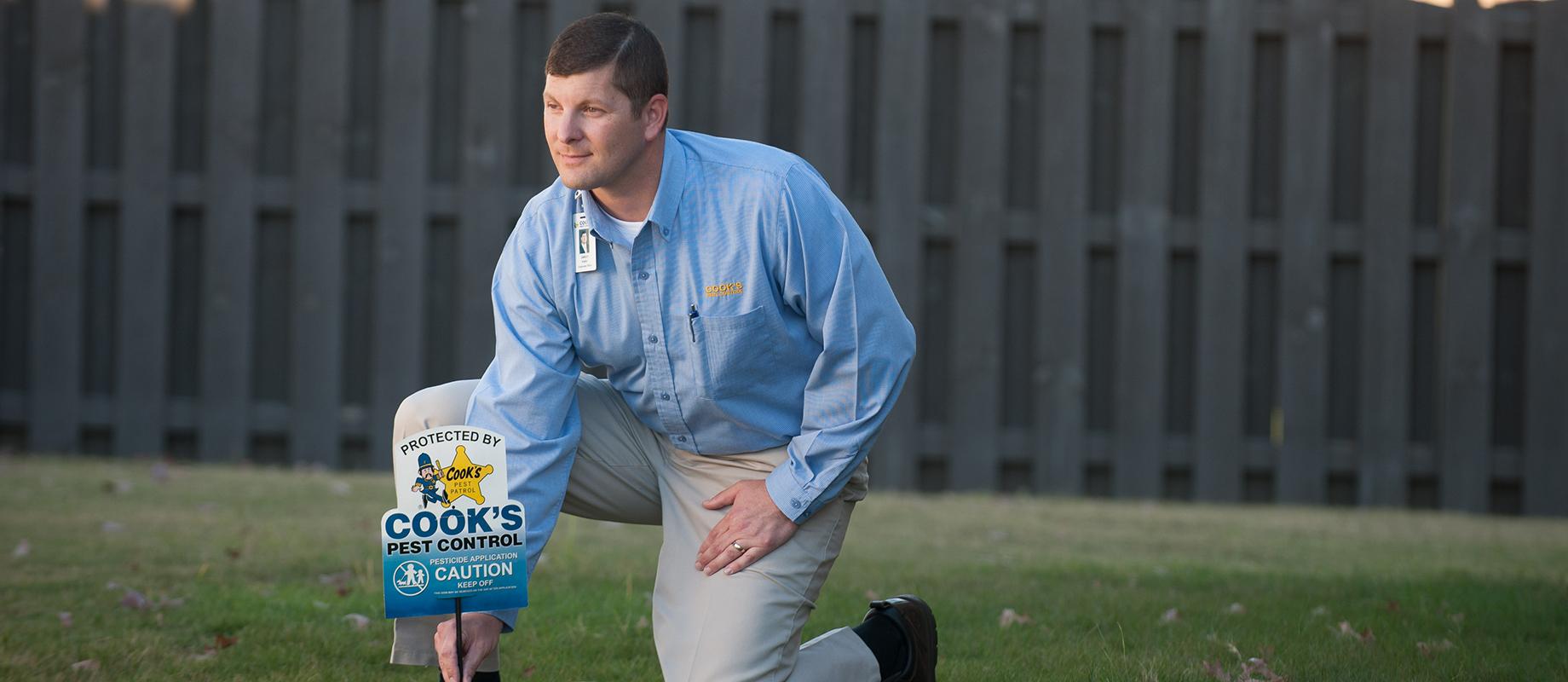 Cook's Pest control professional installing a termite monitoring station on a lawn.