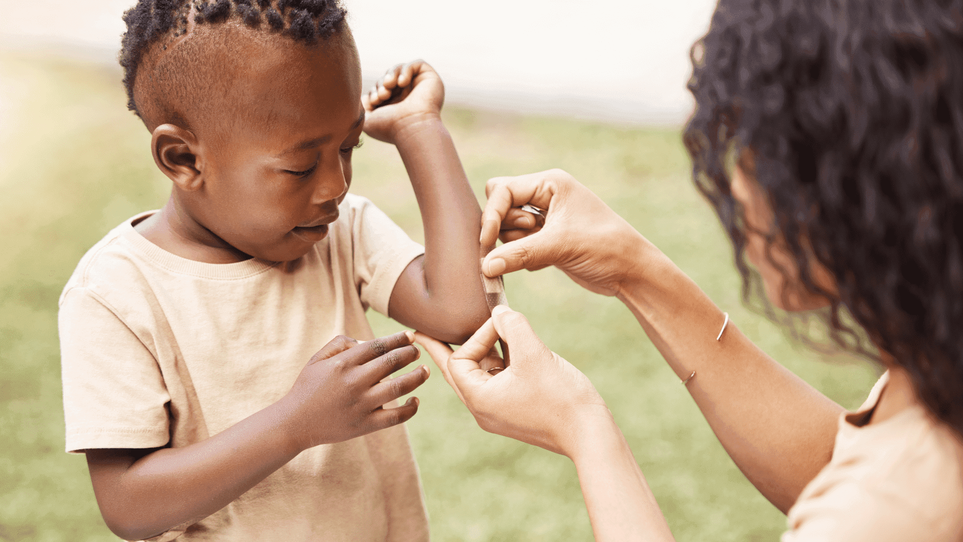 A young child receives a bandage on their arm from an adult, illustrating attentive care for summer bug bites.